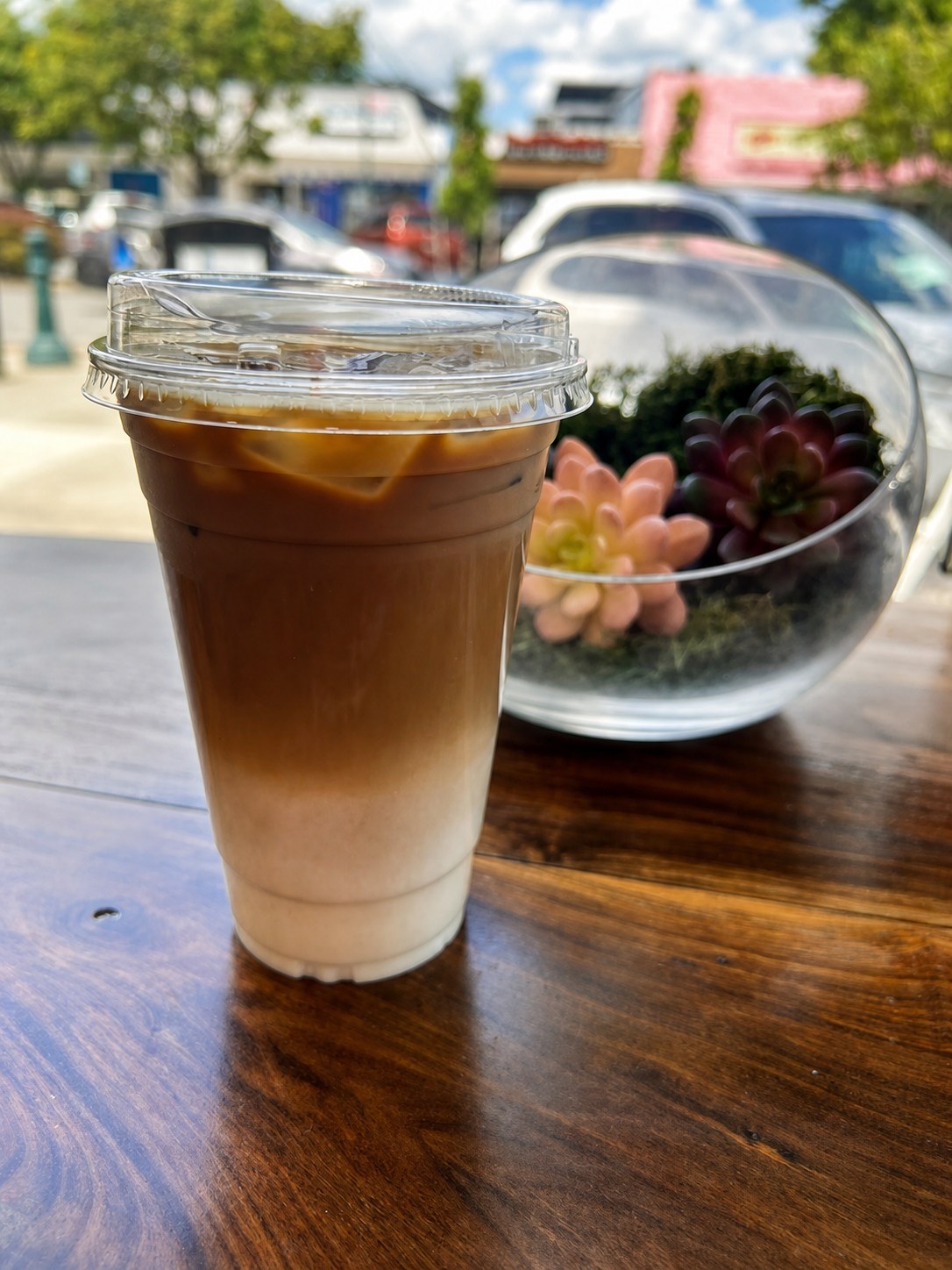Iced latte with distinct milk-and-espresso layers on a wooden table by the window