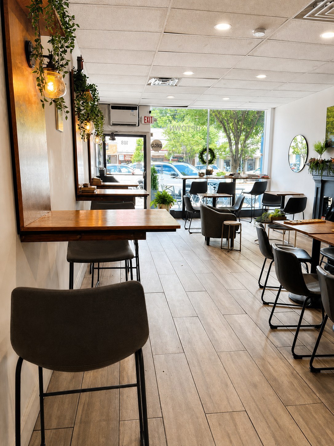 The café's window bar seating with warm wall lamps, hanging plants, and a view of Pleasant Ave