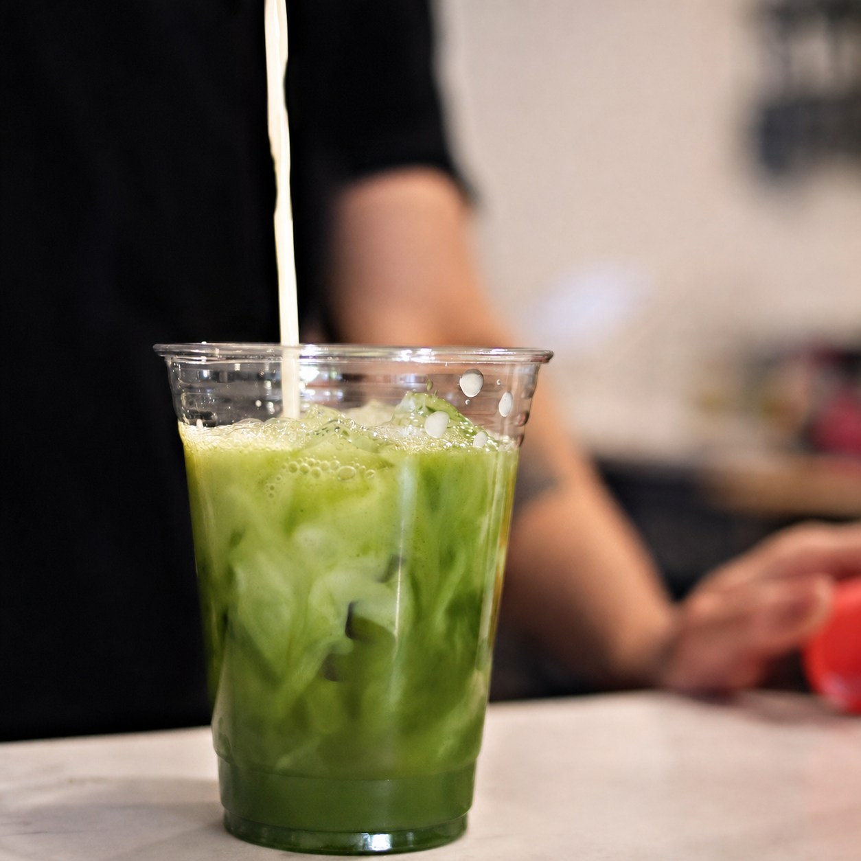 Milk being poured into an iced matcha at the counter