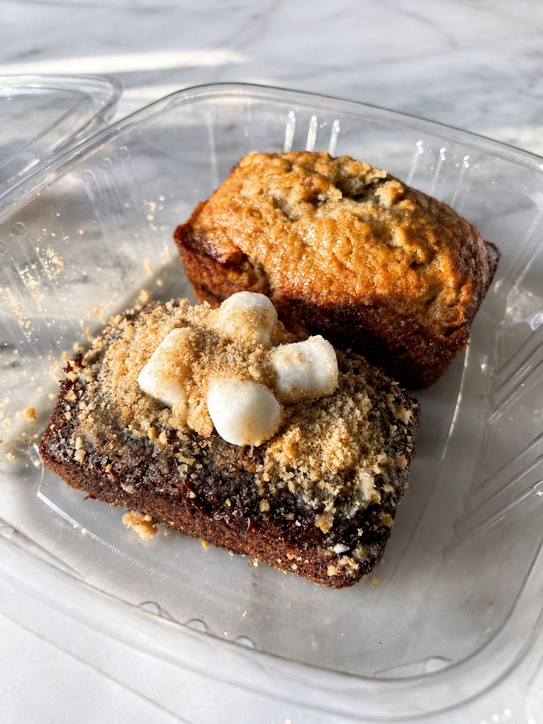 S'mores banana bread topped with toasted marshmallow and graham crumb beside banana nut bread